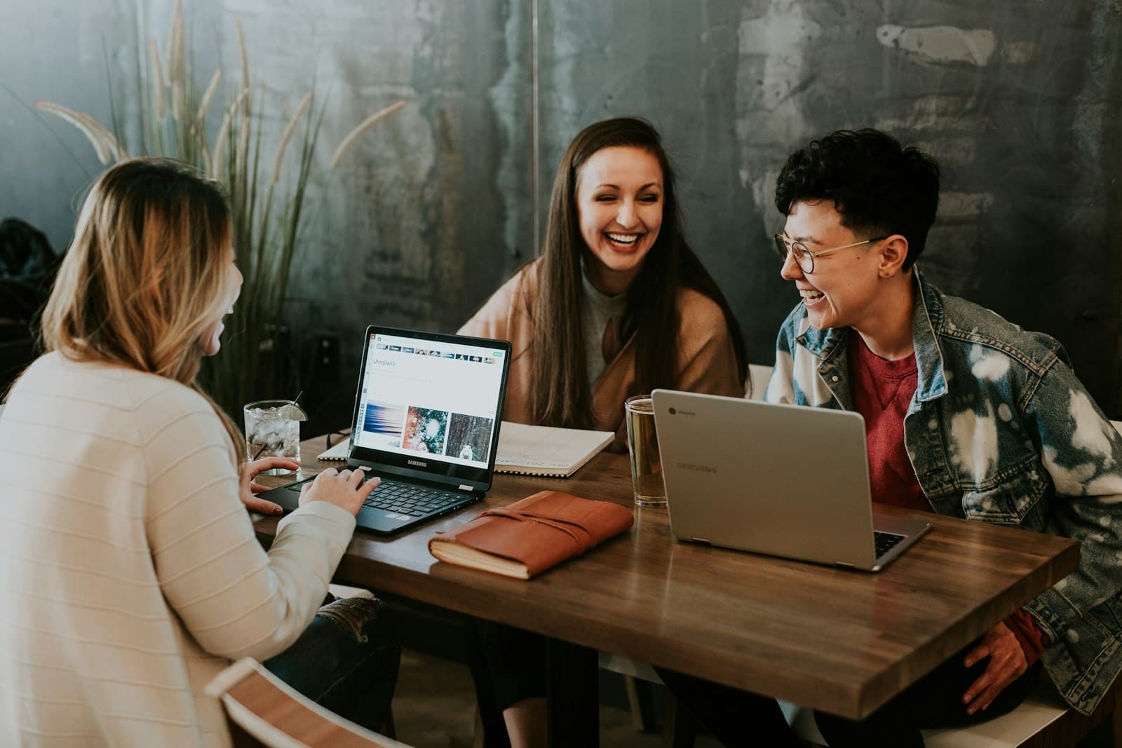 Three people laughing together over laptops at a shared table